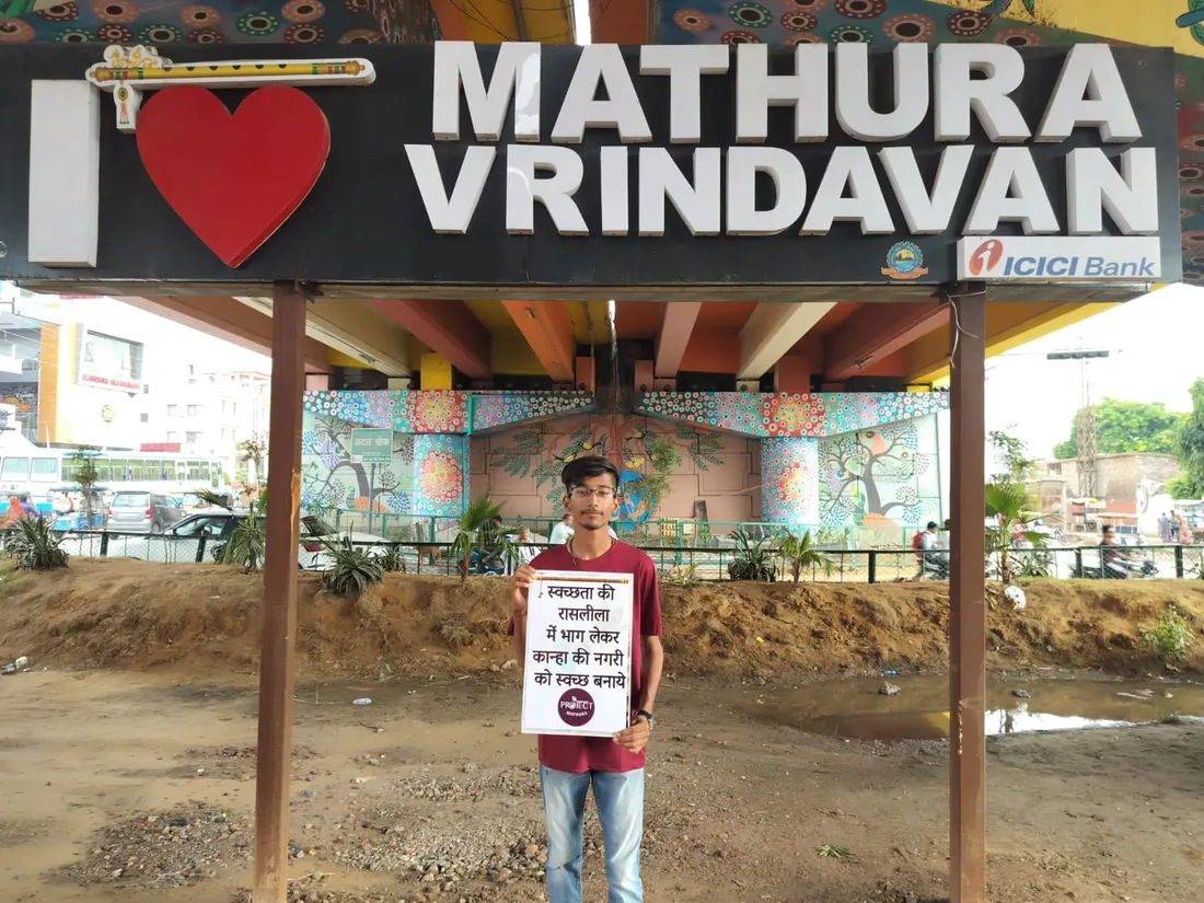 Sarwang Shukla holding a cleanliness campaign placard under the I love Mathura Vrindavan sign